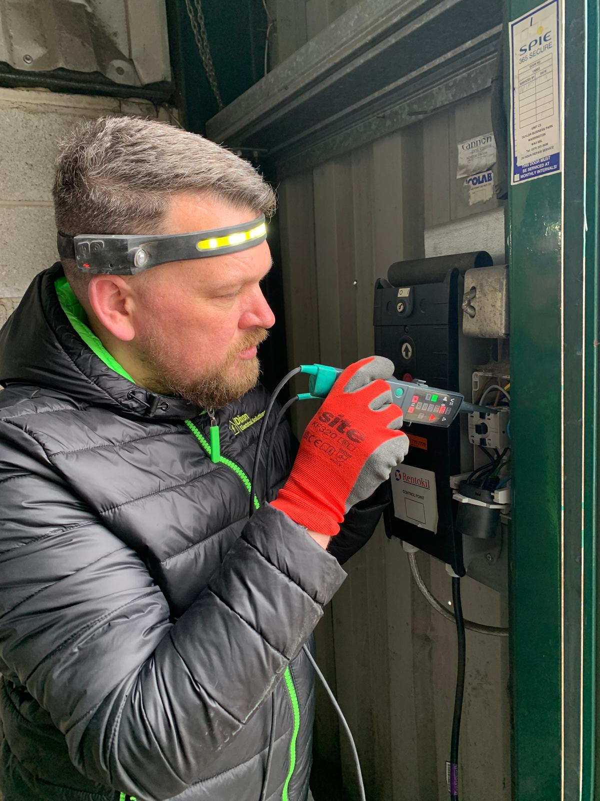 Steven Dixon performing a commercial electrical inspection with multimeter, head torch and PPE gloves at a Yorkshire site