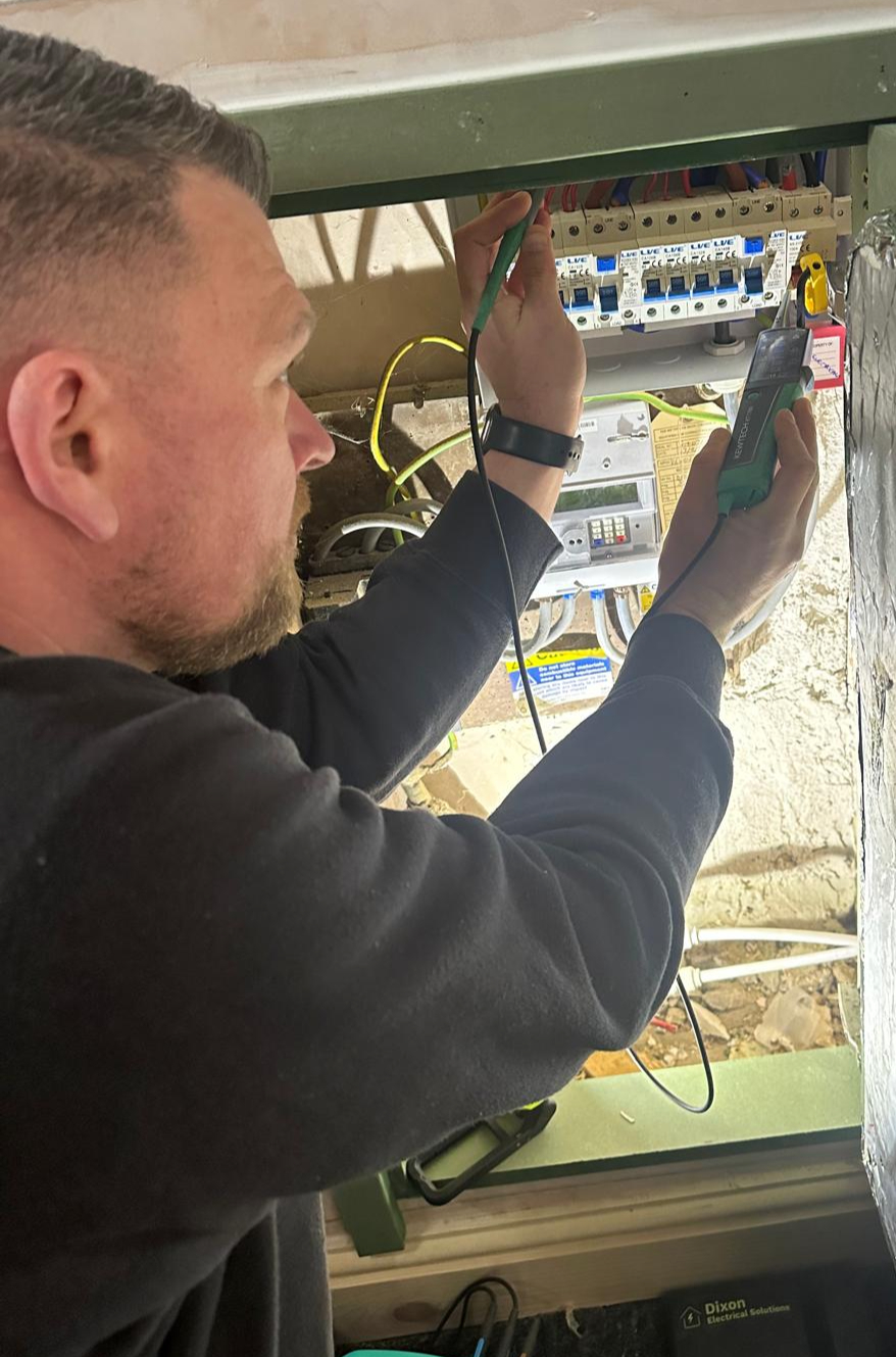 Steven Dixon testing a domestic consumer unit with a multimeter during a fuse-board upgrade